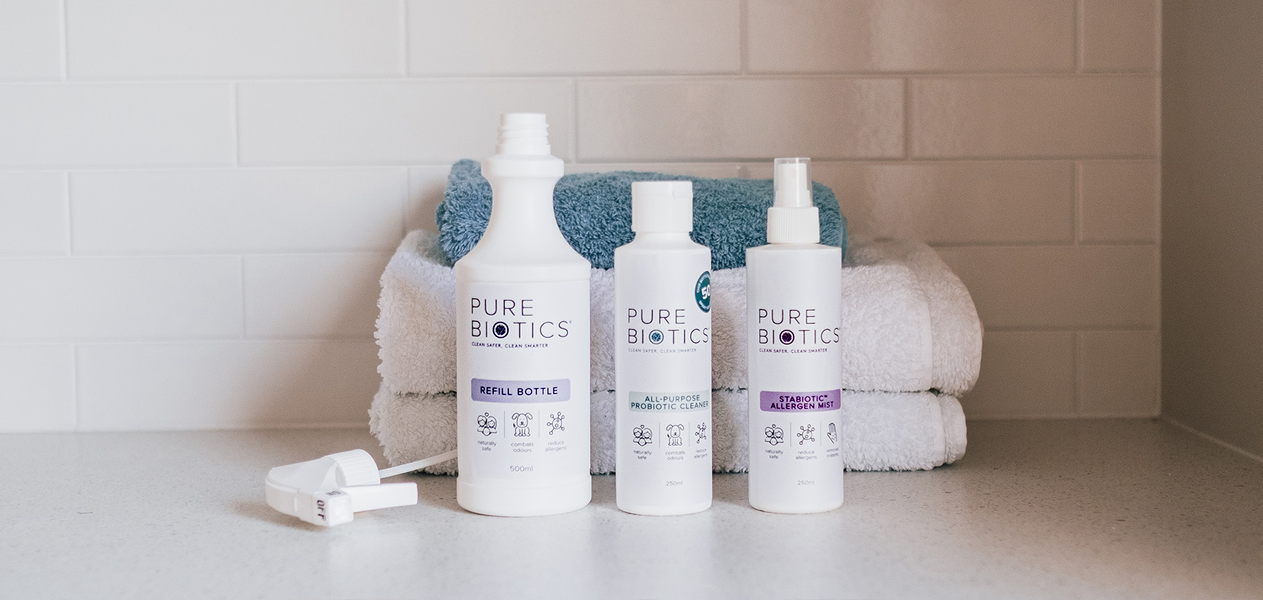 Pure Bitoics cleaning range, 3 white bottles with green and purple logos on them standing in front of a white tiled wall